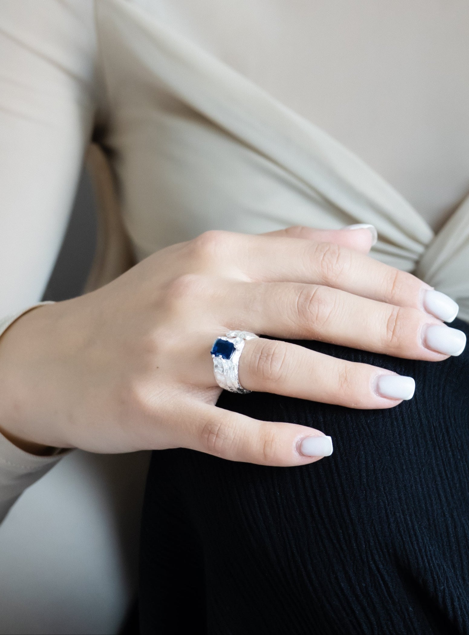 Woman wearing a ring with a blue gemstone and a necklace, sitting on a chair.